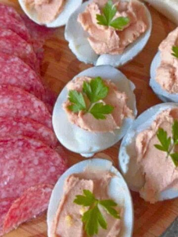 Deviled eggs, salami, cheese, tomatoes, olives, and egg spread on bread arranged on a plate.