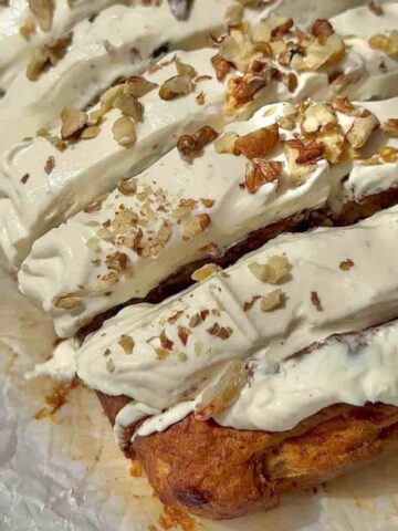 Vegan carrot cake banana bread topped with cream cheese frosting, walnuts.