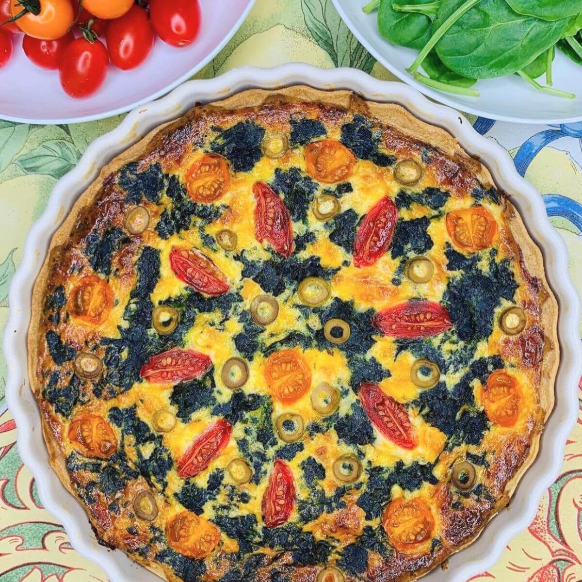 Easy spinach cherry tomato quiche in white ceramic dish with fresh leaves.