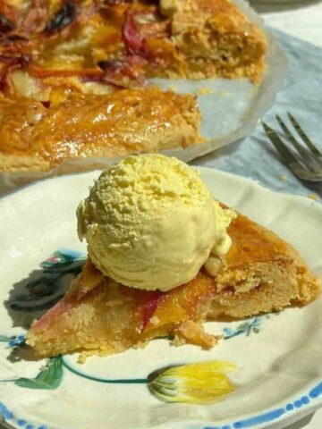 Golden peach galette with brown sugar crust, sliced open to show almond filling and peaches, served with a scoop of vanilla ice cream.